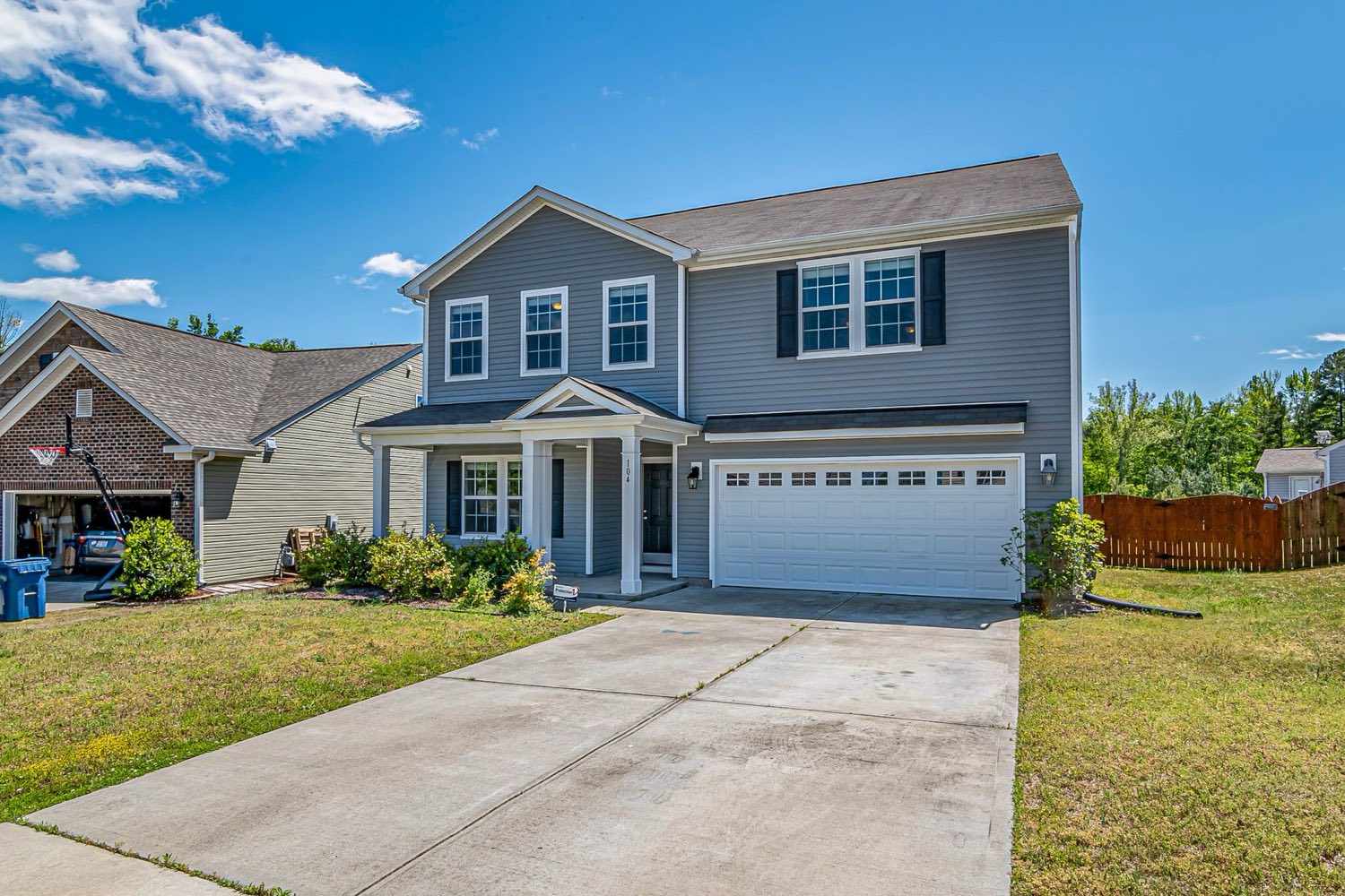 Two-story home with a broom-finished concrete driveway under a bright sky